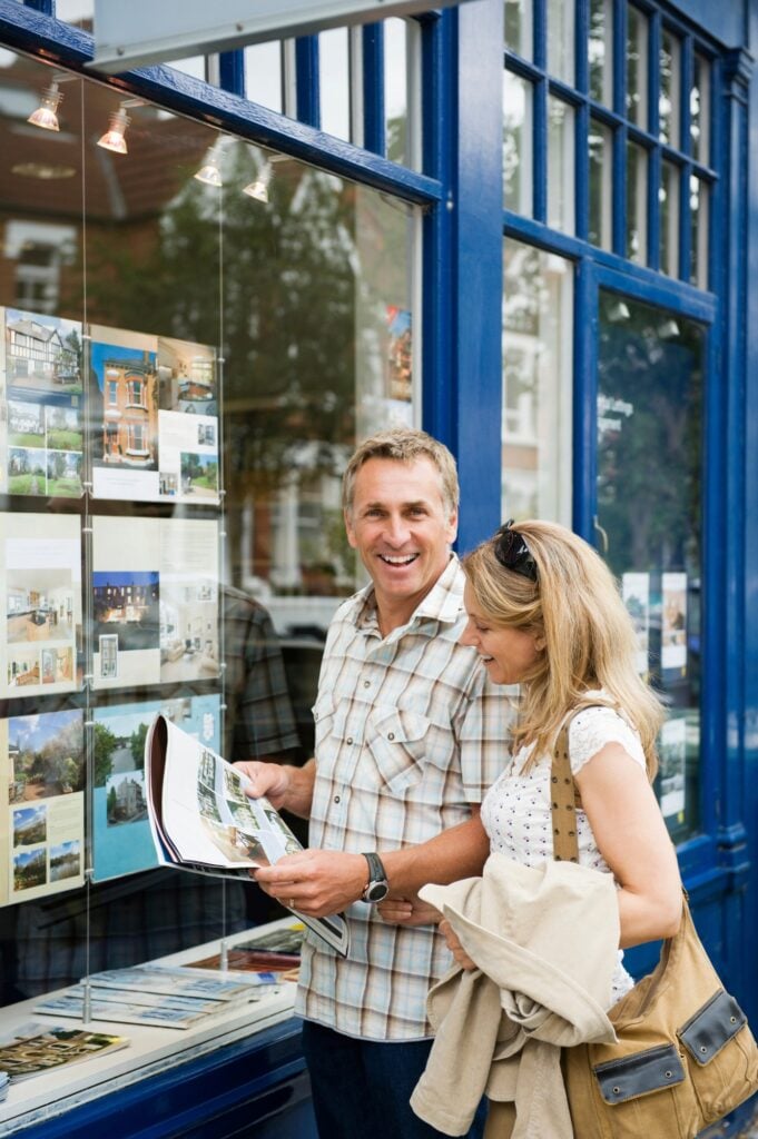 A couple browsing property listings at a real estate office window.